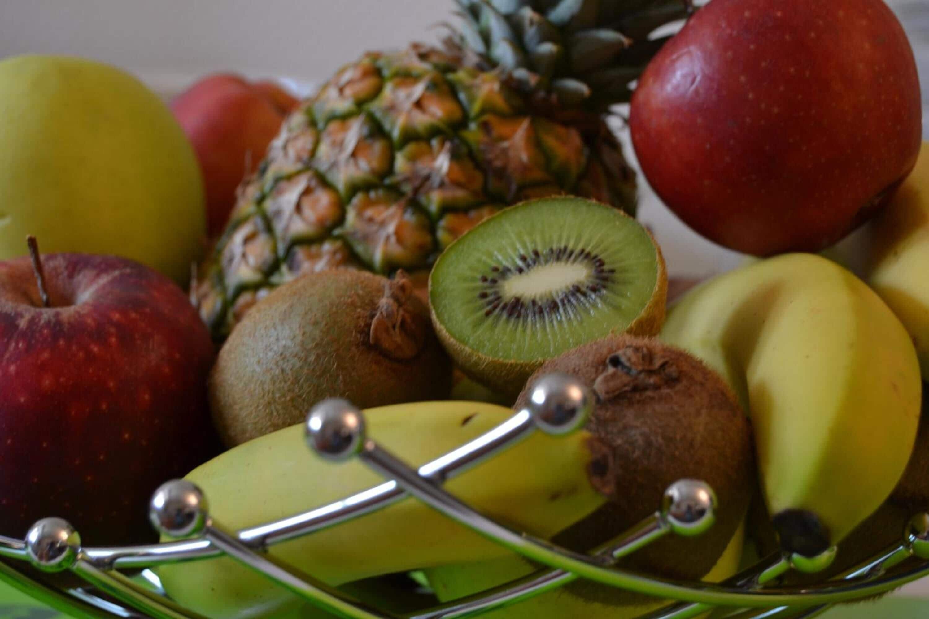 Una cesta de frutas con manzanas, plátanos, una piña y un kiwi.