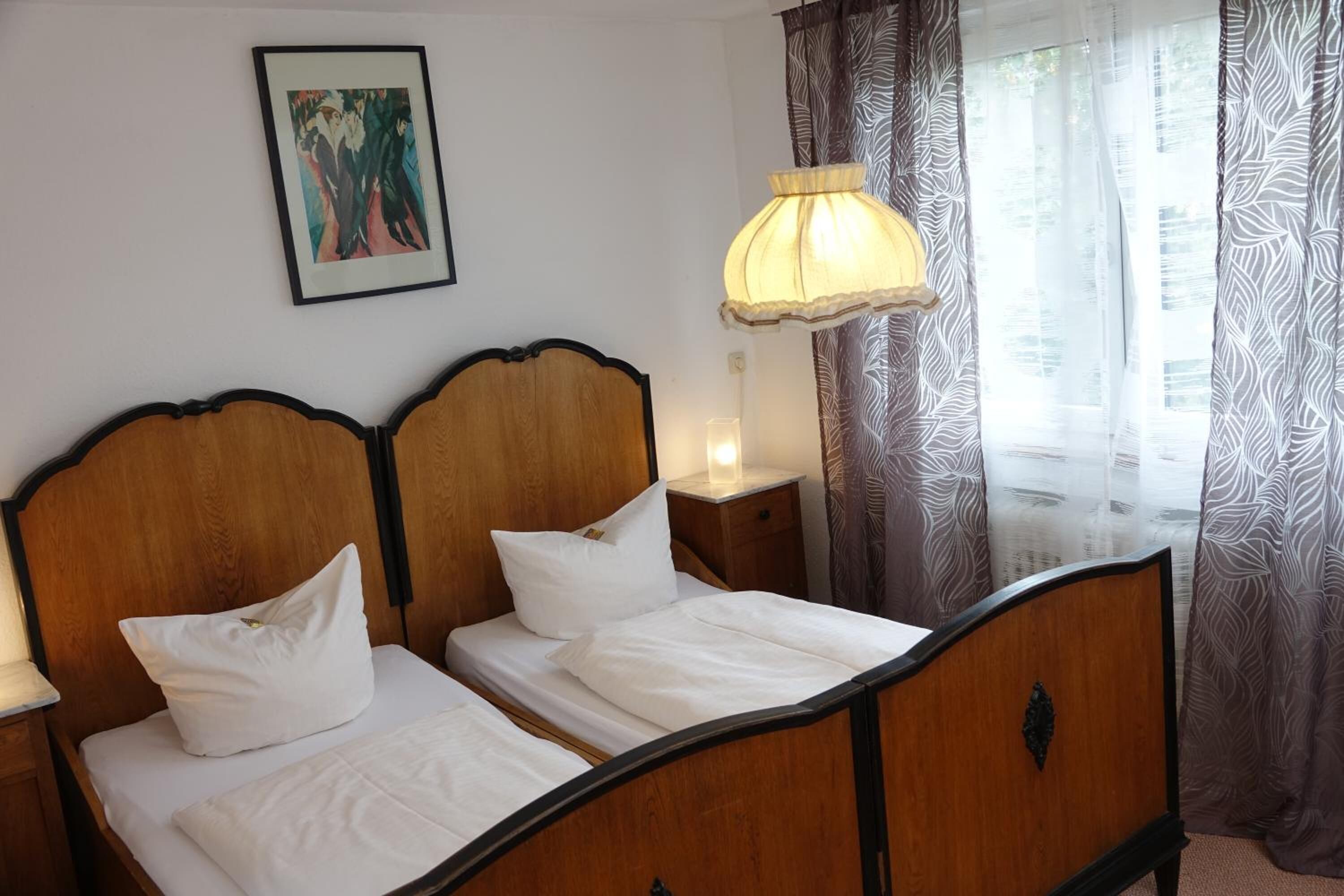 Una cama doble con cabecera de madera, ropa de cama blanca, una mesita de noche con lámpara y una obra de arte enmarcada en la pared.
