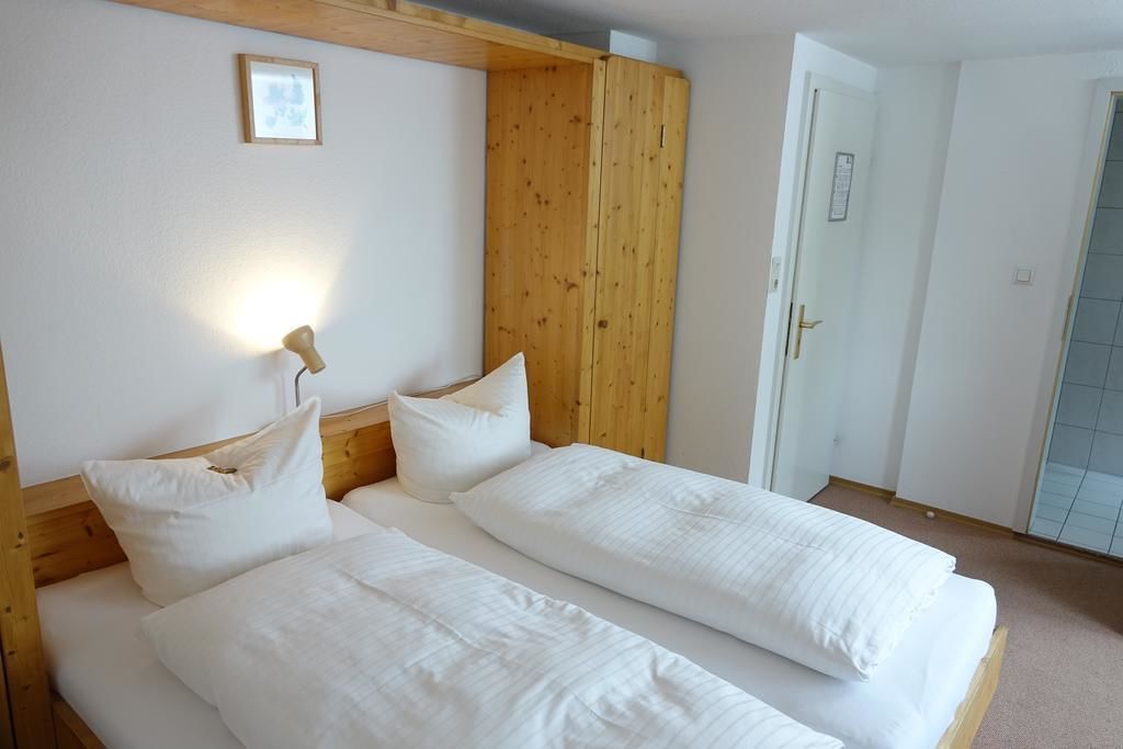 A room with two single beds, wooden headboard, white bedding, a bedside lamp, and a door with a sign.