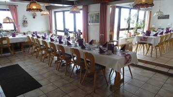 Un espace repas avec plusieurs tables dressées pour le service, des chaises en bois et des lampes suspendues.