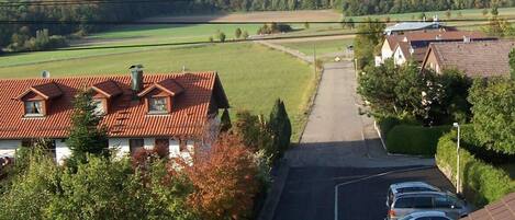 A residential street with houses on both sides, parked cars, and a clear view of the countryside.