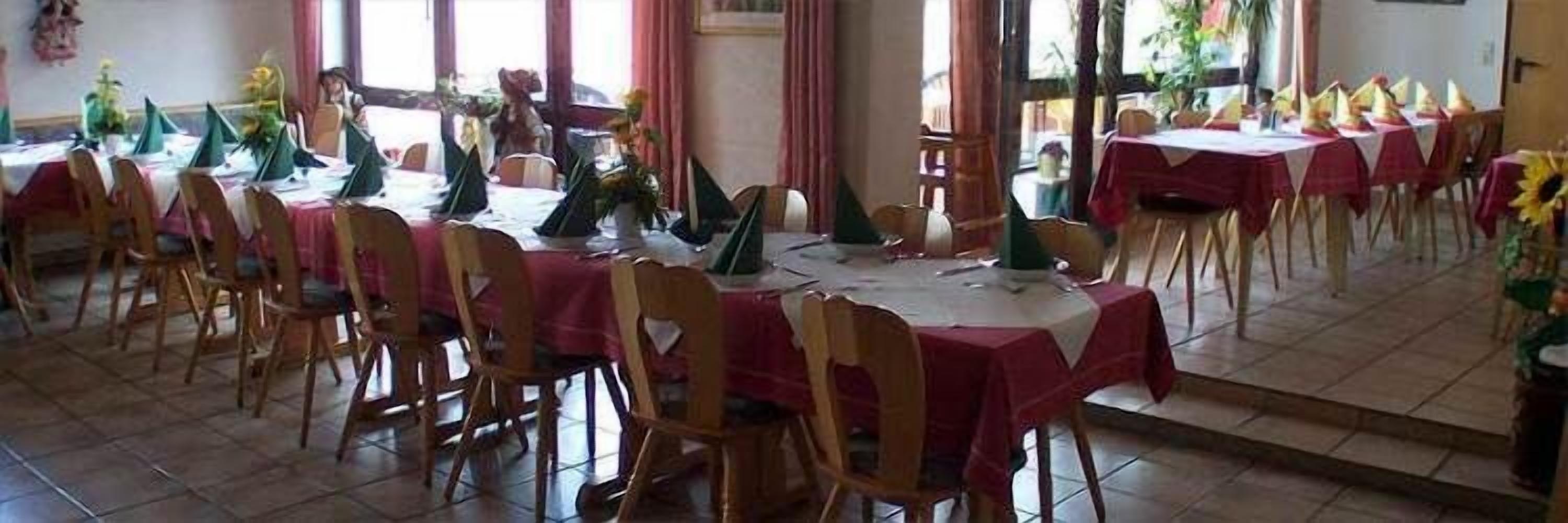 A dining area with multiple tables covered with red tablecloths and wooden chairs.