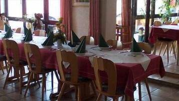 A dining area with multiple tables covered with red tablecloths and wooden chairs.
