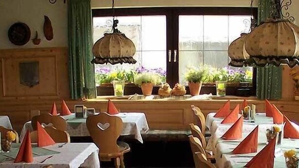 A restaurant with tables set for dining, a large window with plants, and hanging lamps. - Landgasthof Metzgerei Traube (Heidenheim an der Brenz)