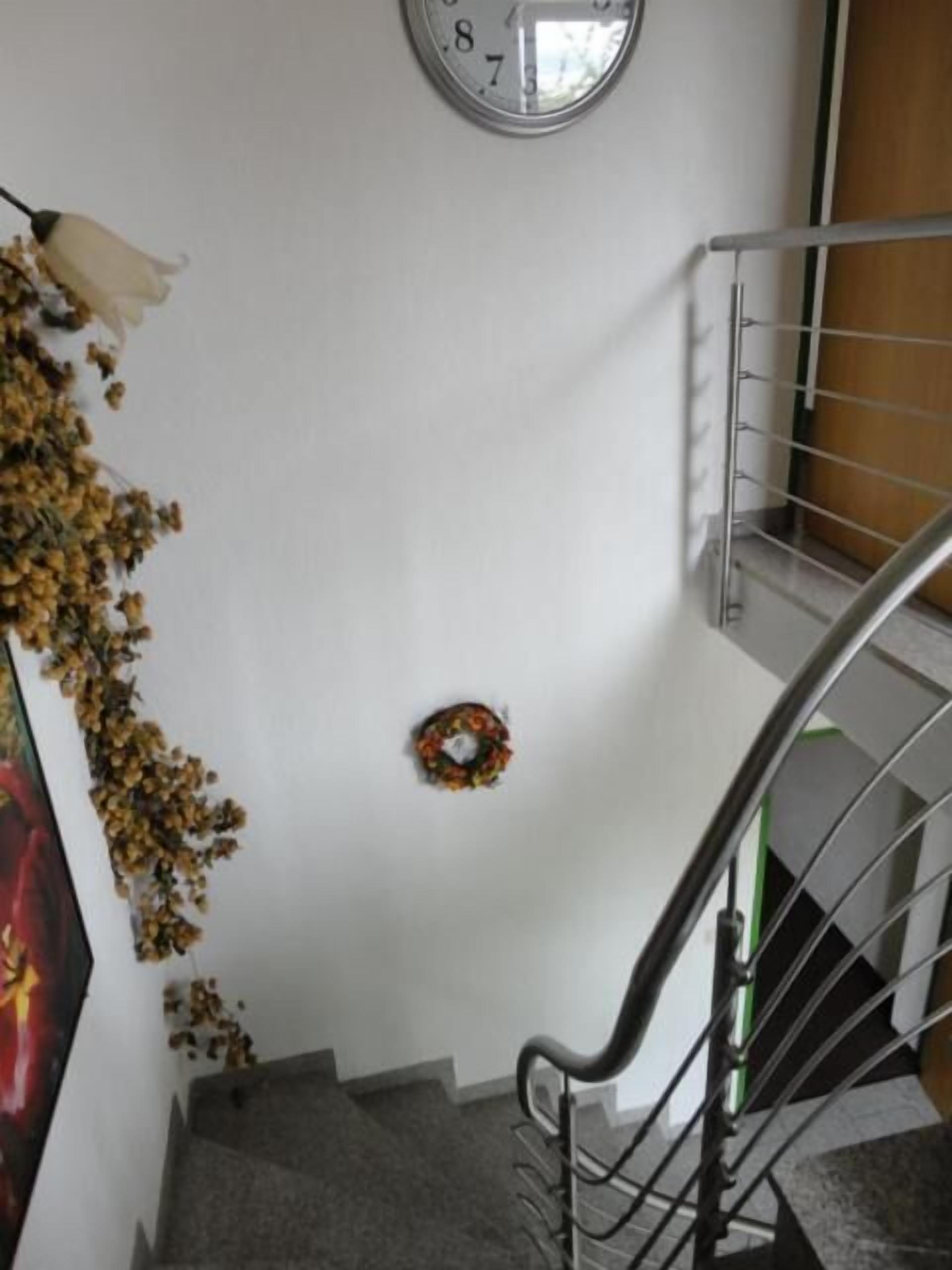 A staircase with a metal handrail, a wall clock, and a wreath on the landing.