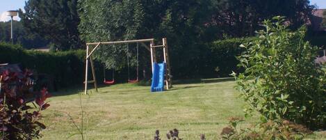 A grassy outdoor area with a swing set and a slide.