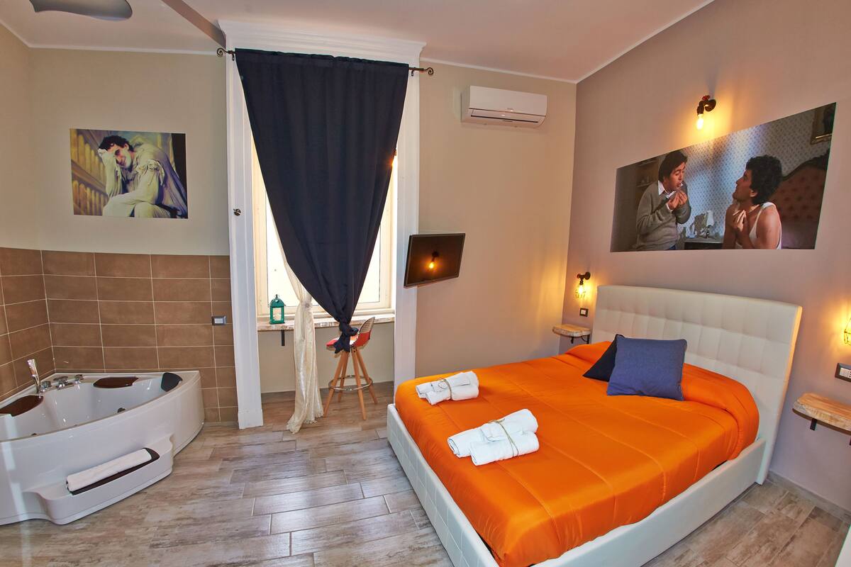 A hotel room with a large bed, an en-suite bathroom, and artwork on the walls.