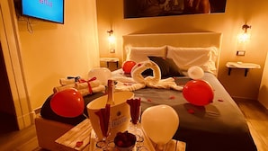 A hotel room with a bed, a TV displaying 'NETFLIX', a bottle of champagne, balloons, and a tray with a cake and glasses. - Artisti Bed&Dreams (Naples)