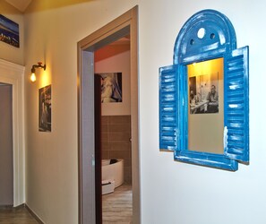 A hallway with a blue-framed mirror, a door leading to a bathroom, and a wall-mounted light fixture. - Artisti Bed&Dreams (Naples)