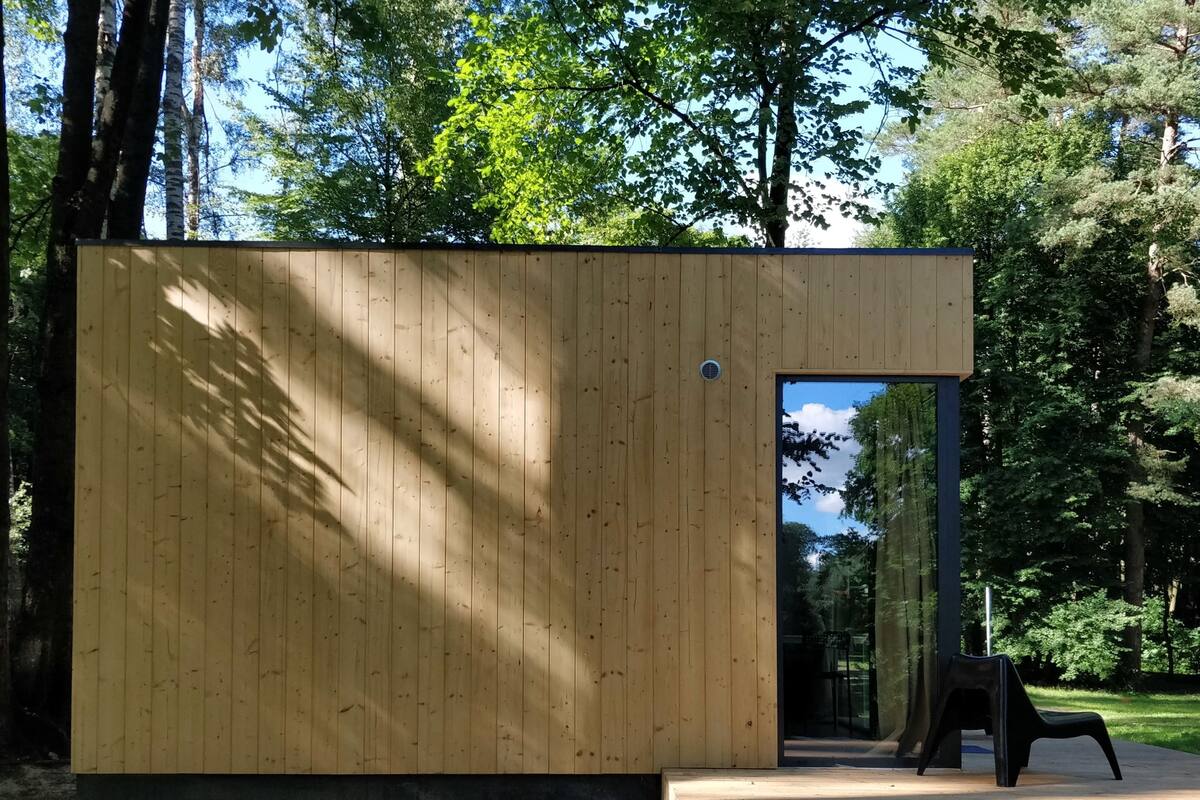 Una cabaña de madera con una puerta que da a un espacio interior, rodeada de árboles.