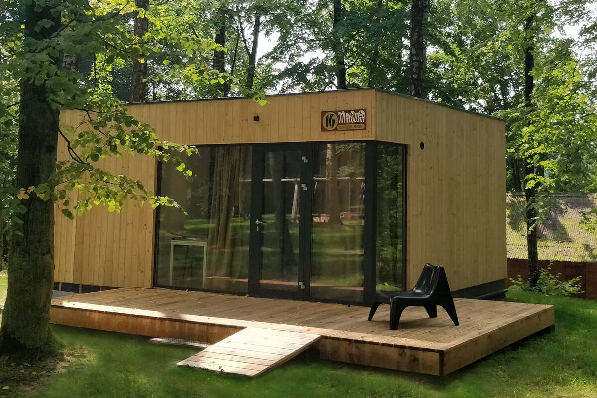 Una pequeña cabaña de madera con puerta de vidrio, un banco y una terraza de madera.