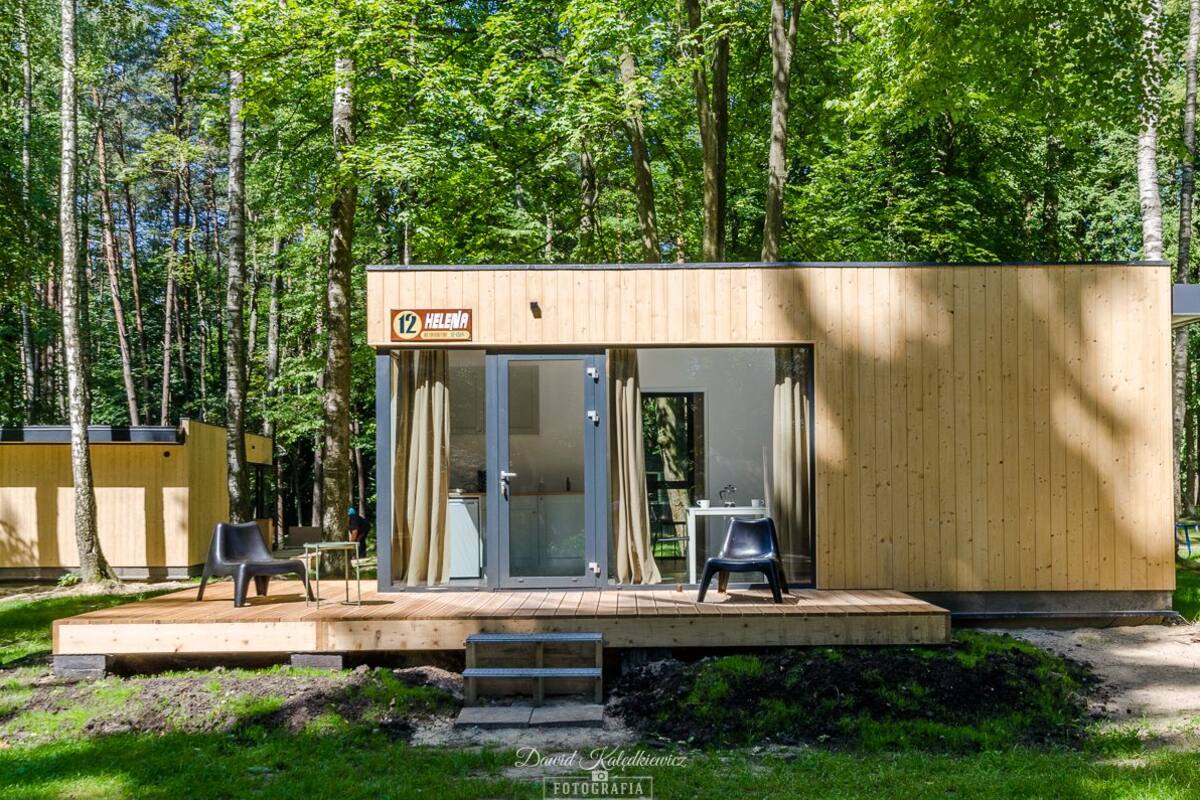 Una pequeña cabaña de madera con puerta de vidrio, una terraza con dos sillas y un cartel que indica una sauna.