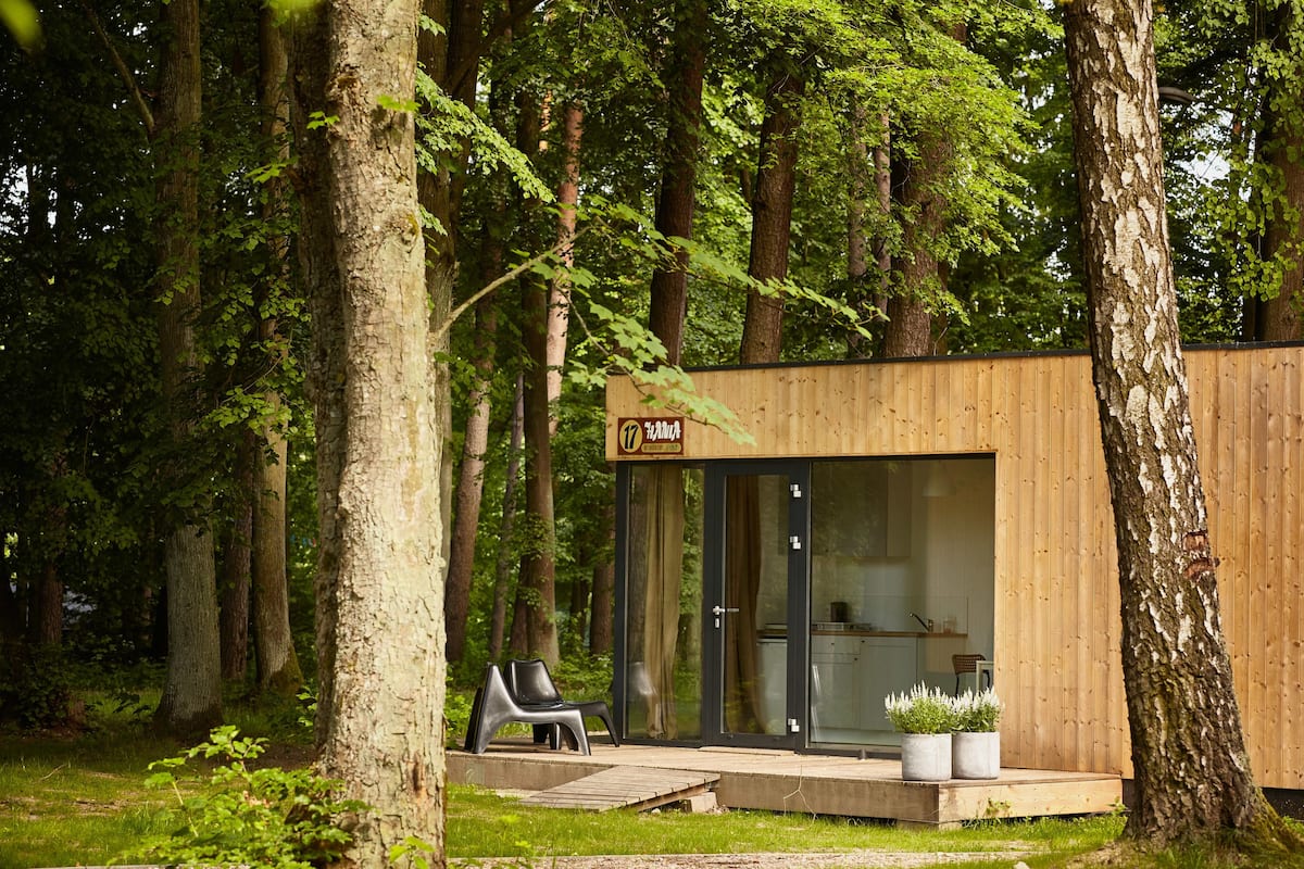 Una cabaña de madera moderna con puerta de vidrio, rodeada de árboles.