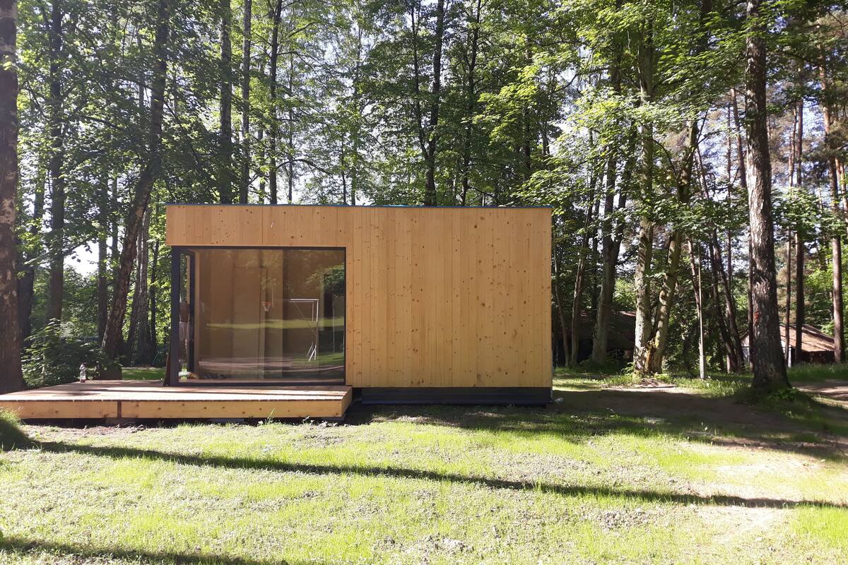 Una cabaña moderna de madera con puerta de vidrio, rodeada de un bosque.