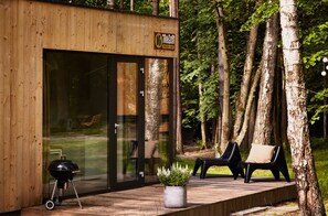 A wooden cabin with a glass door, a barbecue grill, and two black chairs on a deck. - Kaletka (Ilawa)