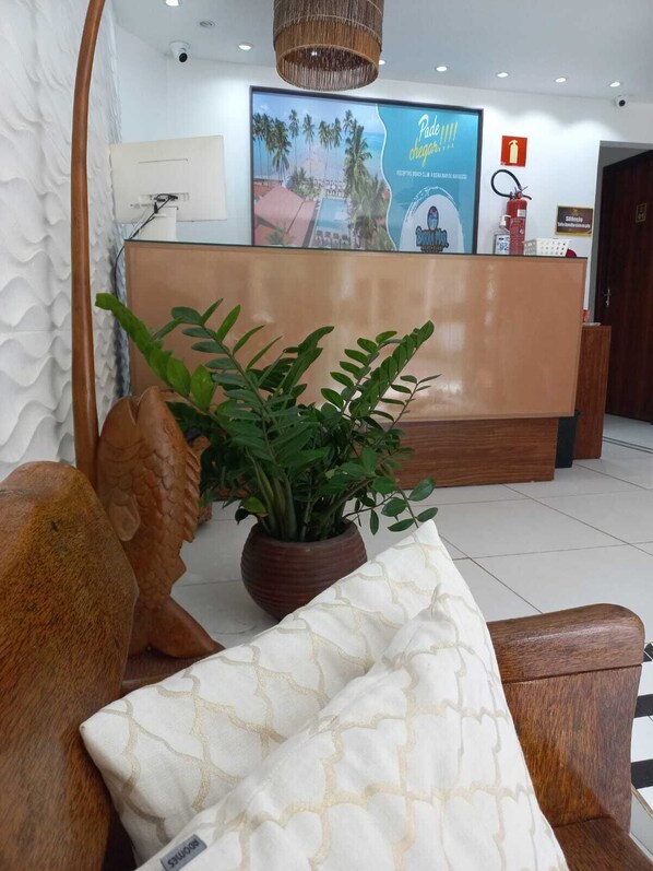 A reception desk with a poster, a potted plant, and a wooden sculpture. - Pousada dos Cabanos (Maragogi)