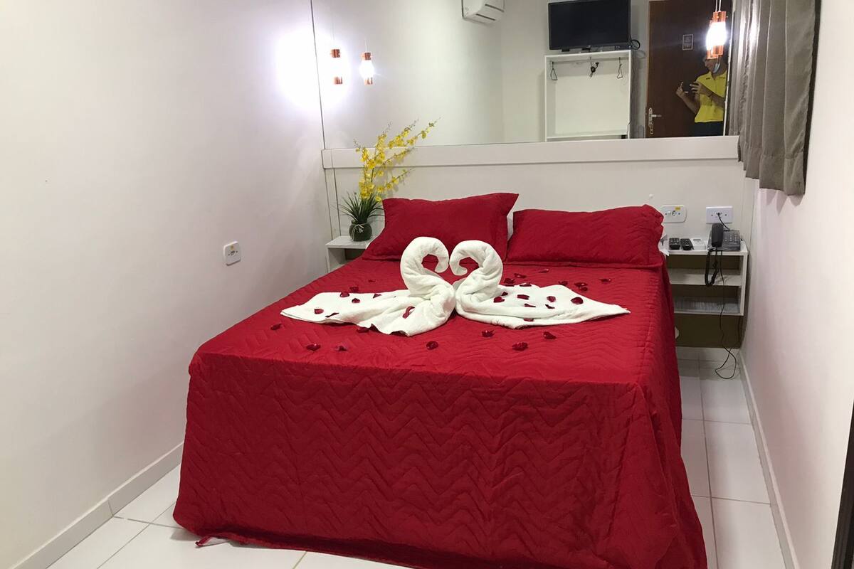 A neatly made bed with a red bedspread and a decorative swan towel arrangement.