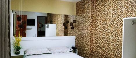 A hotel room with a bed, a bedside table with a lamp, a mirror, and a wall with a pixelated pattern.
