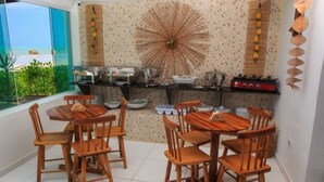 Un espace repas avec des tables et des chaises en bois, une cuisine équipée et une vue sur l’océan.