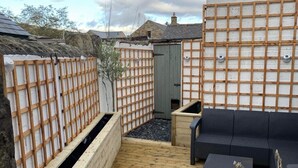 A wooden deck with a black sofa and a small table, surrounded by a wooden fence and a green door.