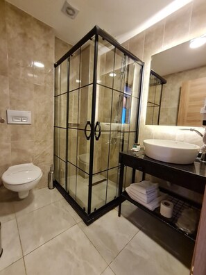 Une salle de bain moderne avec une douche à parois de verre, des toilettes blanches, un lavabo avec un miroir et un porte-serviettes.