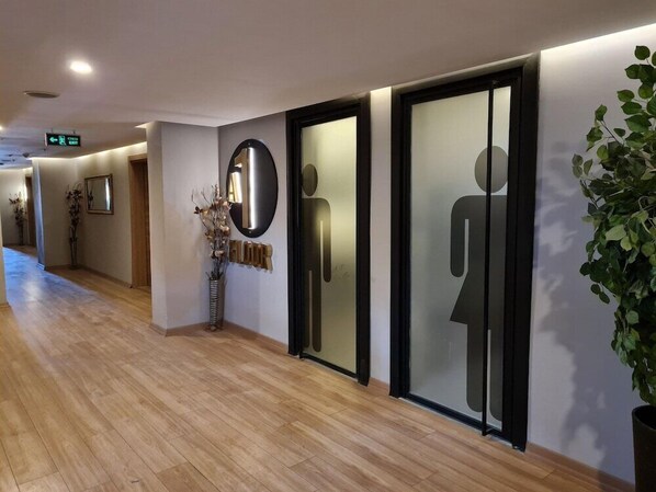 Un couloir doté d’un plancher en bois, d’un miroir, d’une plante et d’un panneau fixé au mur indiquant une sortie.