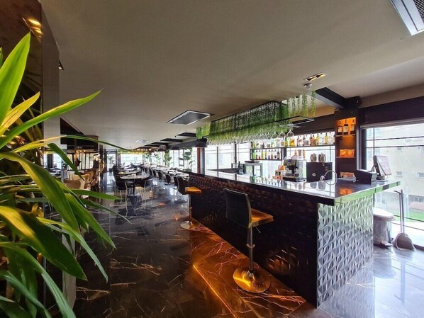 Un espace bar moderne doté d’un comptoir en verre, de sièges et offrant une vue sur la ville.