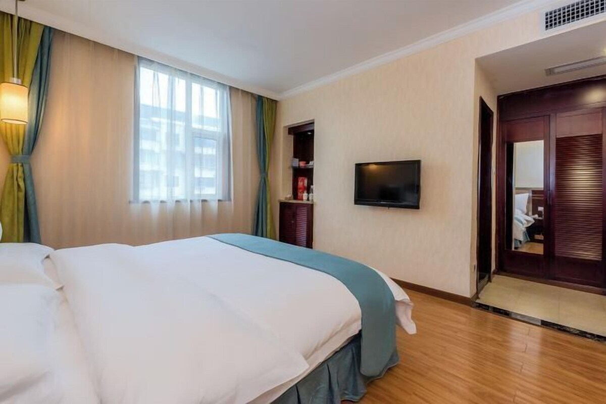 A hotel room with a bed, a television, a wardrobe, and a window with curtains.