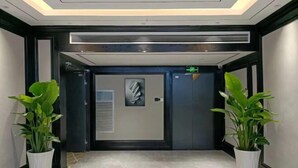 A modern hallway with a marble floor, a black door with a glass panel, and two potted plants. - Jincheng Hotel (Zunyi)