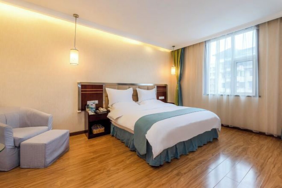 Habitación de hotel con cama, mesita de noche, lámpara, silla y ventana con cortinas.