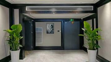A hallway with a door, potted plants, and a ceiling light fixture.