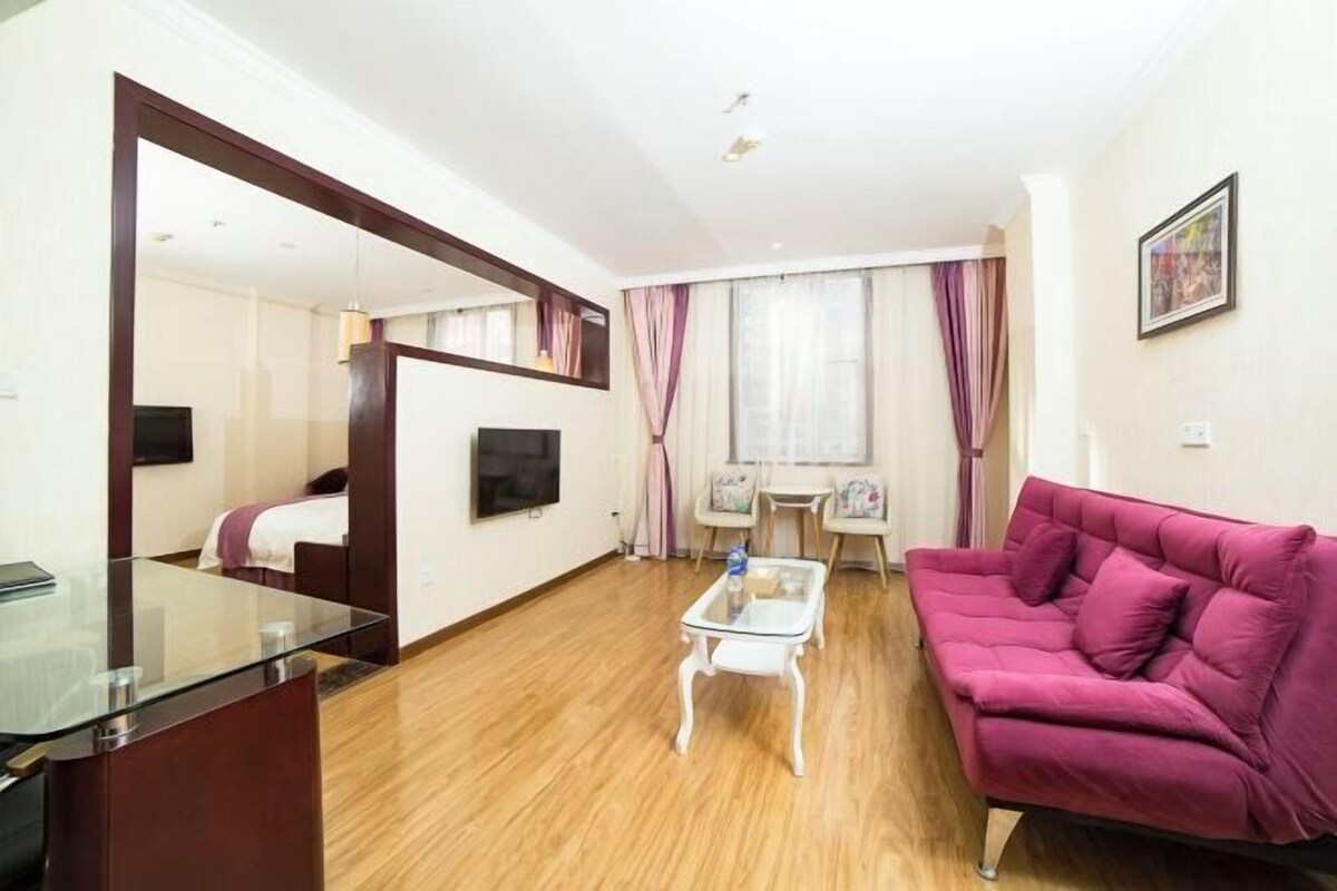 A modern hotel room with a glass dining table, a pink sofa, a TV, and a large mirror.