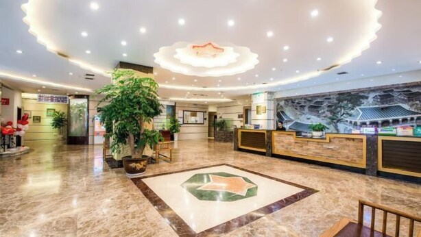 A hotel lobby with a reception desk, a large potted plant, a decorative floor design, and a mural on the wall. - Jincheng Hotel (Zunyi)