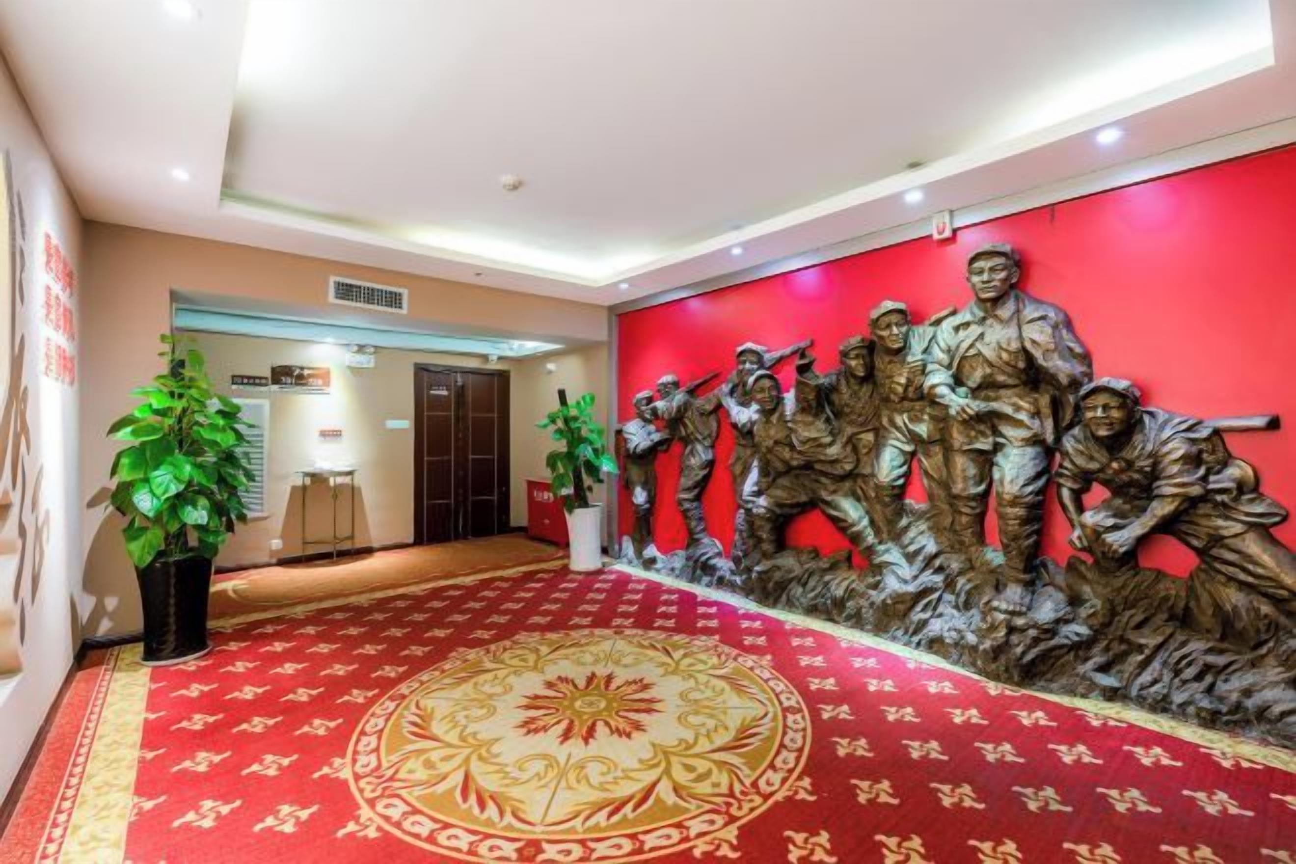 A hotel lobby with a red carpet, a reception desk, and a wall-mounted sculpture of soldiers.