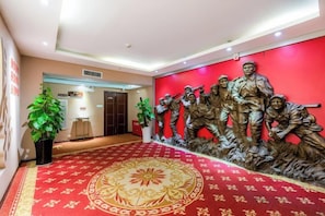 Vestíbulo de hotel con alfombra roja, una recepción y una escultura de soldados en la pared.