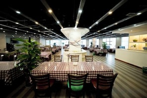 Un restaurante espacioso con varias mesas y sillas, una columna decorativa central y un techo bien iluminado.