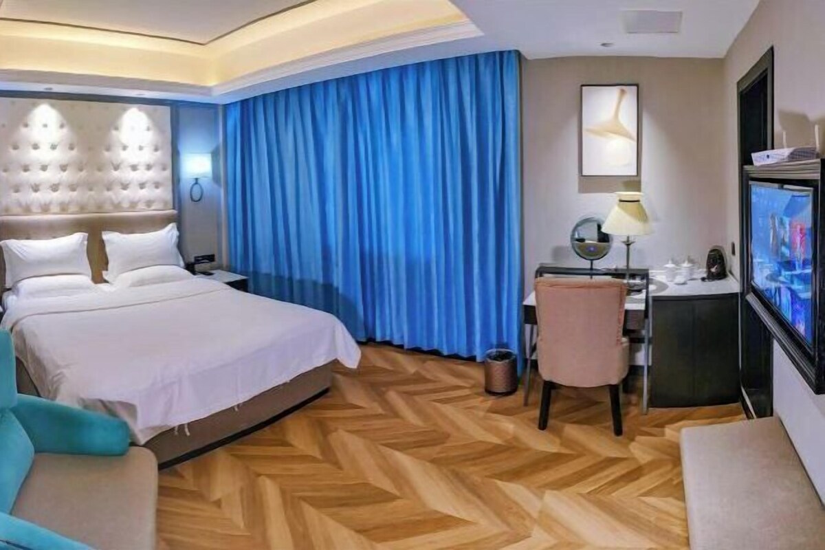 A hotel room with a large bed, a desk with a computer, a TV, and a chair.