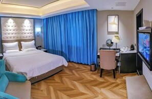 A hotel room with a large bed, a desk with a computer, a TV, and a chair.