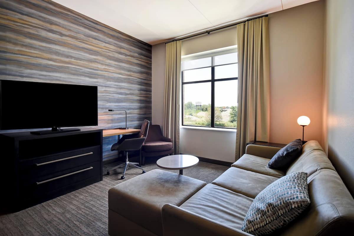 A modern hotel room with a flat-screen TV, a sofa, a coffee table, and a desk with a chair.