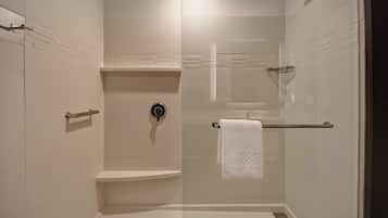 A modern shower area with a glass door, a white towel hanging on a rack, and a toilet with a shelf above it.