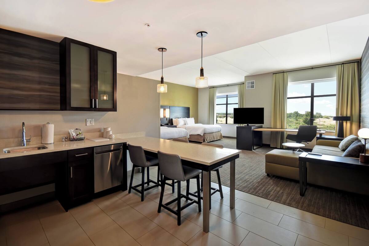 A hotel room with a kitchenette, a dining area, a bed, a TV, and a view of the outdoors.
