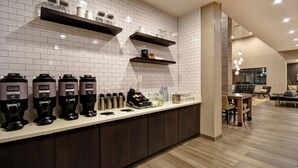 A modern kitchen with coffee makers, shelves with glassware, and a dining area with a table and chairs. - Residence Inn by Marriott Cincinnati Northeast/Mason (Mason)