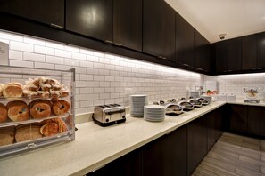 A modern kitchen with dark cabinets, a white tiled backsplash, and a breakfast display with pastries and a toaster. - Residence Inn by Marriott Cincinnati Northeast/Mason (Mason)
