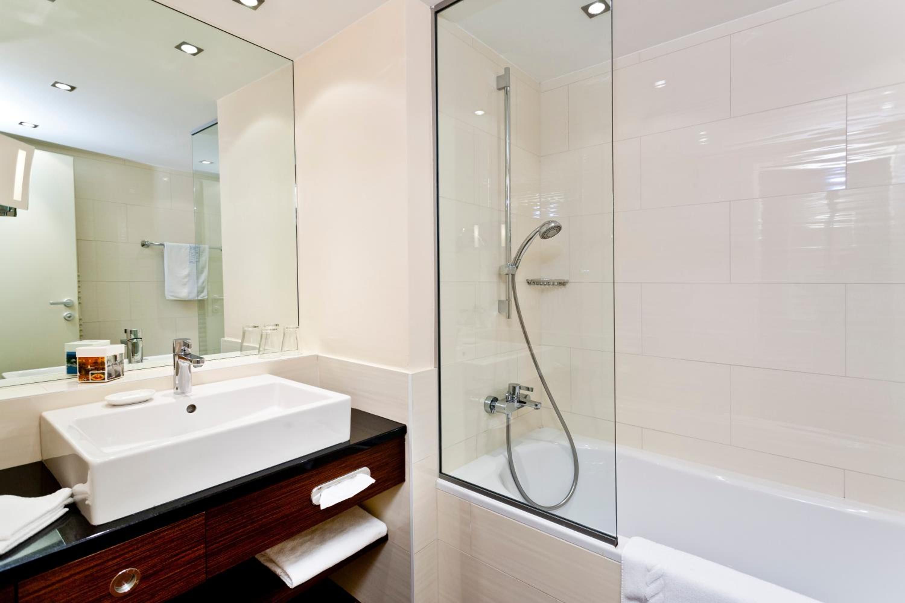 Un baño moderno con un lavabo, tocador y zona de ducha con mampara de vidrio.