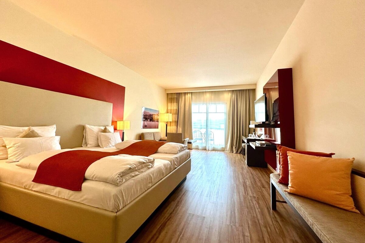 A hotel room with a large bed, a desk, a chair, and a television.