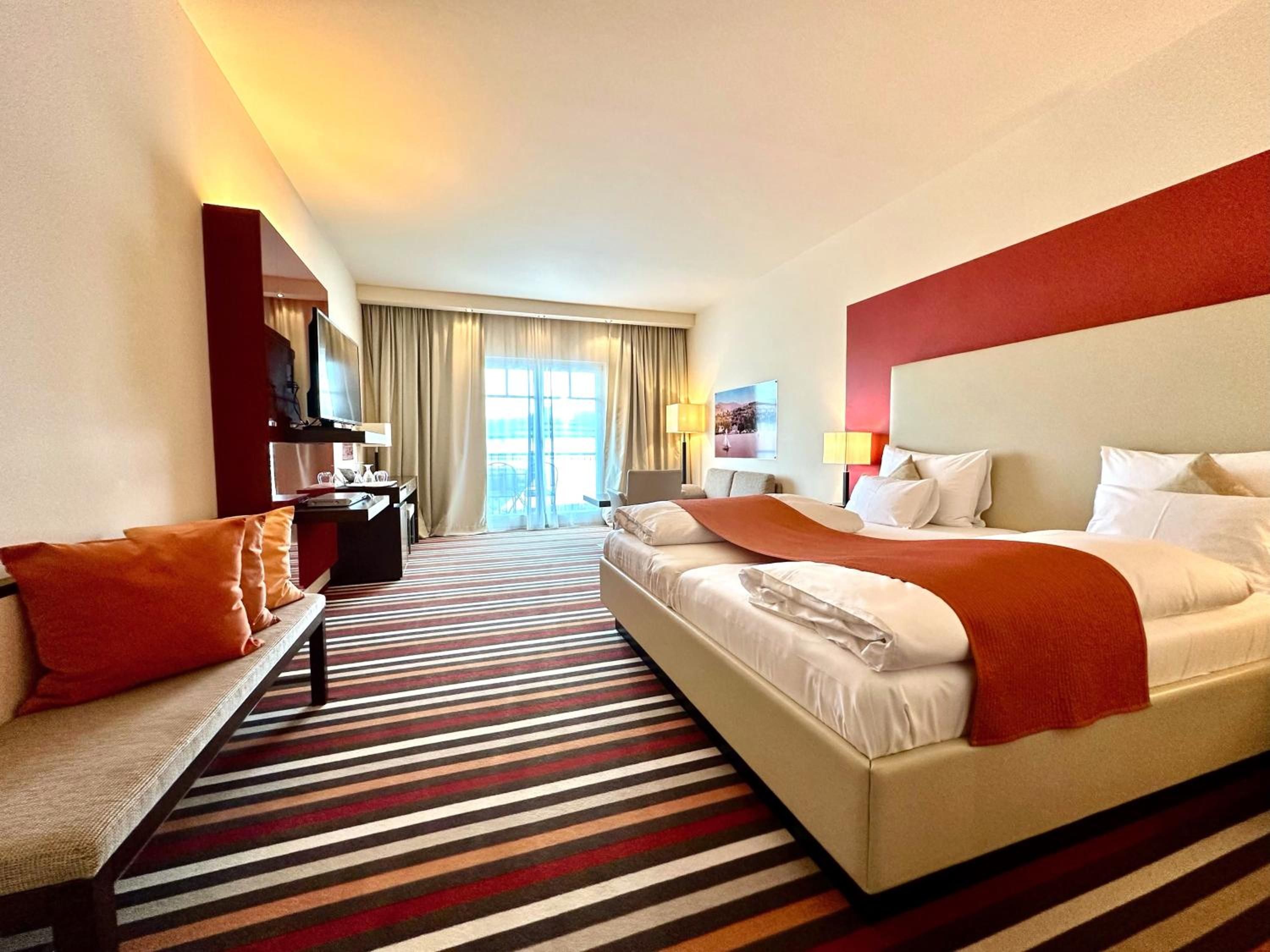 Una habitación de hotel con cama, escritorio, silla, sofá y un ventanal con cortinas.
