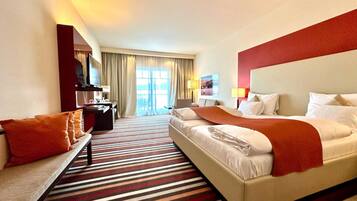 Una habitación de hotel con cama, escritorio, silla, sofá y un ventanal con cortinas.
