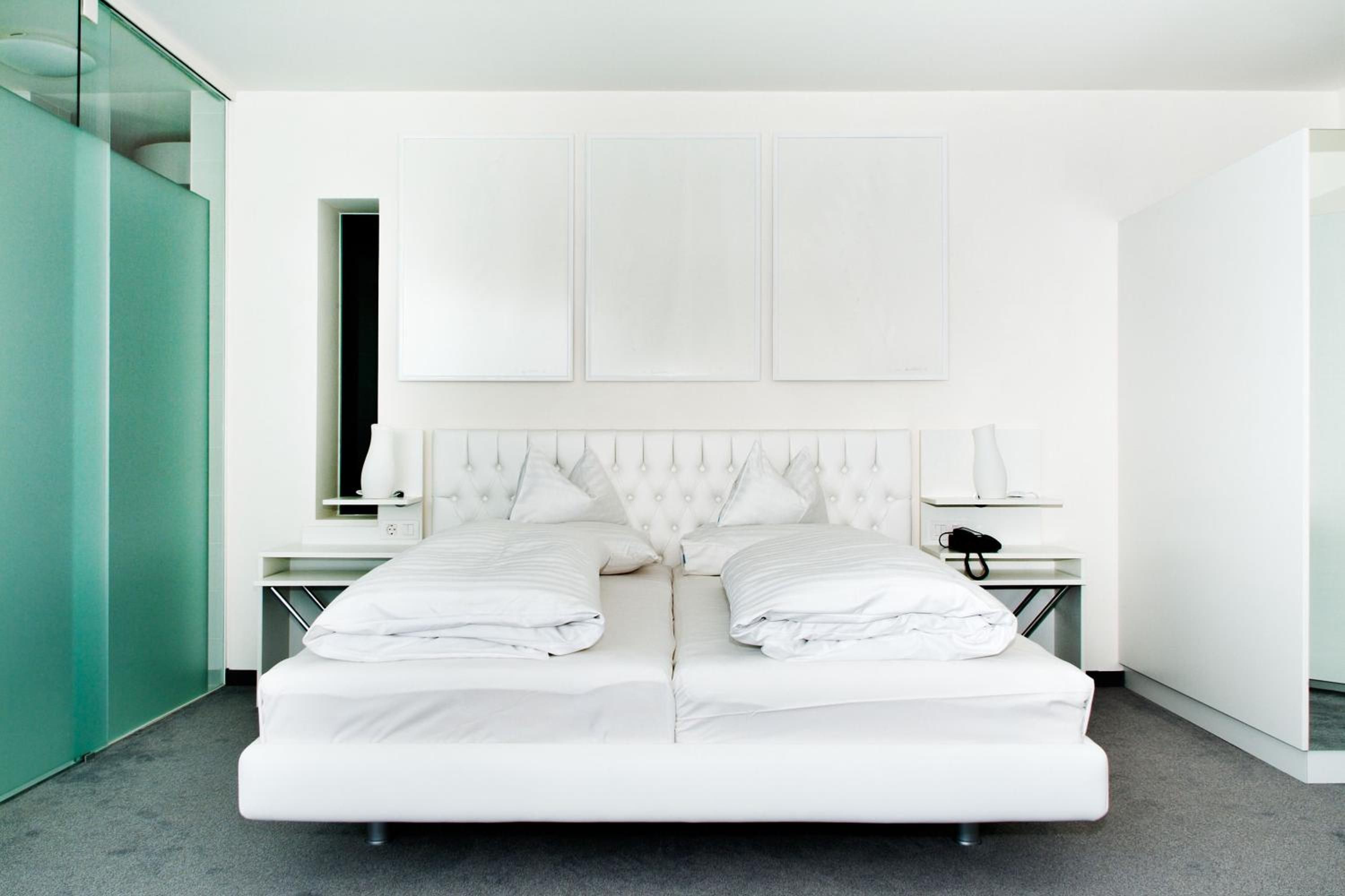 A modern hotel room with a large bed, a bedside table with a lamp, and a small table with a phone.