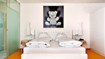 Un dormitorio moderno con una cama grande, un cabecero acolchado, dos mesitas de noche con lámparas y un cuadro en la pared con un osito de peluche.