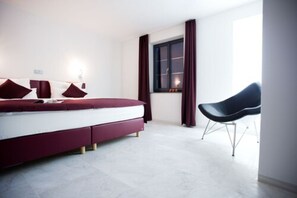 A modern bedroom with a bed, a chair, and a window with curtains. - Hotel Freihof (Prichsenstadt)